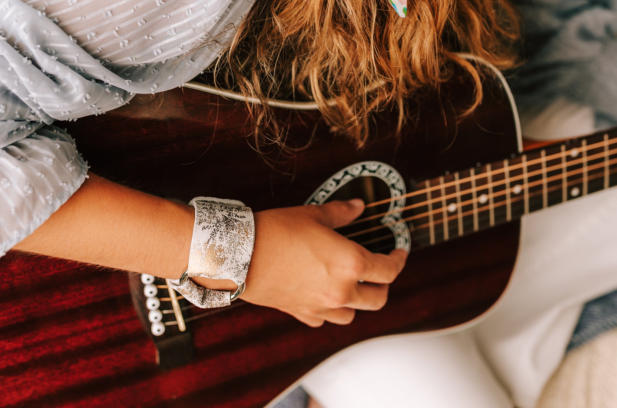 Woman wearing silver and white rustic leather cuff bracelet while playing guitar