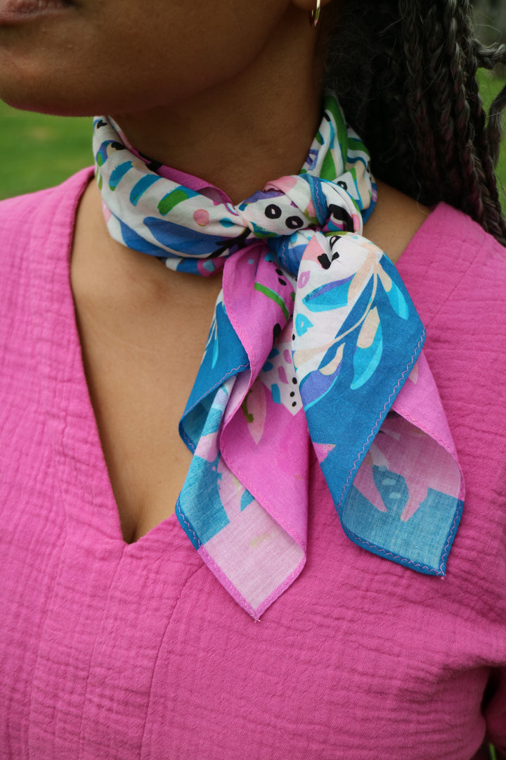 Amina Bandana Scarf designed by Jeanetta Gonzales featuring pink blue and purple floral patterns tied around model's neck